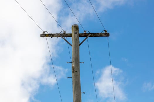 A wooden telephone pole with wires and terminal connectors in front of a bright blue sky background