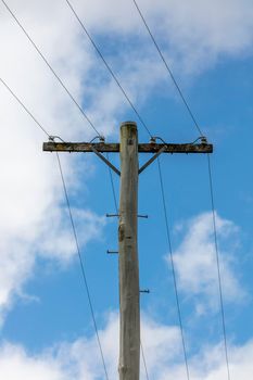 A wooden telephone pole with wires and terminal connectors in front of a bright blue sky background