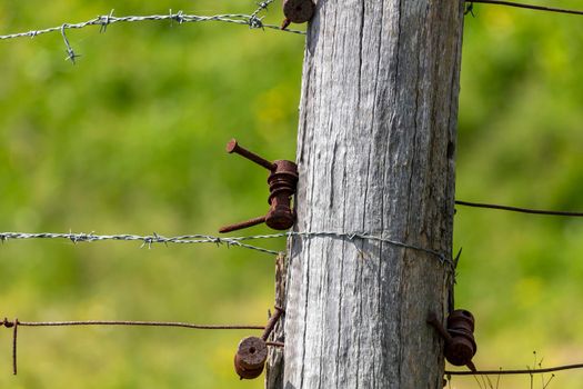 An old agricultural fence post with barbed wire and tension brackets in a field