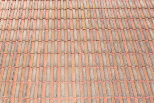 An old brown terracotta tiled roof on a house in the sunshine in summer