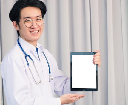 Portrait closeup of Happy Asian young doctor handsome man smiling in uniform and stethoscope neck strap showing front blank screen smart digital tablet on hand, Healthcare medicine concept