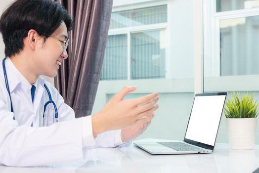 Asian young handsome doctor man wearing a doctor's dress and stethoscope video conference call or facetime raise hand to explain the symptoms he smiling at hospital office, Health medical care concept