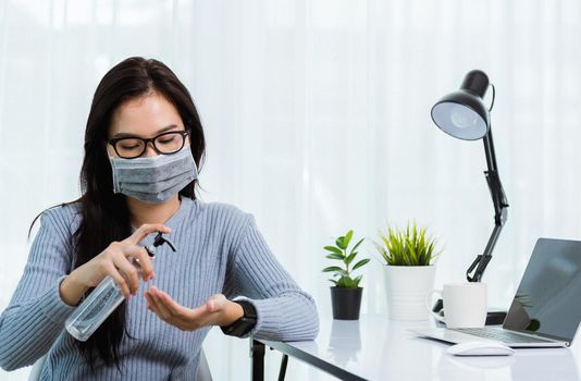 Asian young business beautiful woman wearing face mask protective working from home office with laptop computer desk he quarantines disease coronavirus and cleaning hands by sanitizer alcohol gel pump