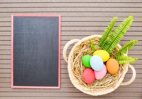 Colorful easter eggs in the basket and blackboard on wood background with space