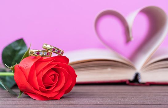 Pages of book curved into a heart shape and red rose. Love concept of heart shape from book pages on pink background