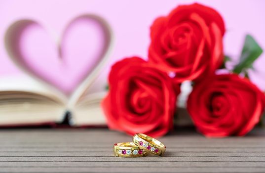 Pages of book curved into a heart shape with red rose and wedding ring . Love concept of heart shape from book pages