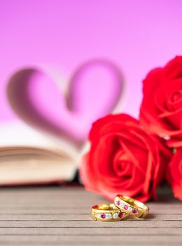 Pages of book curved into a heart shape with red rose and wedding ring . Love concept of heart shape from book pages