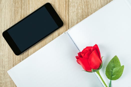 Top view shot of red roses on blank notebook diary and  smartphone on wood table,Valentine concept