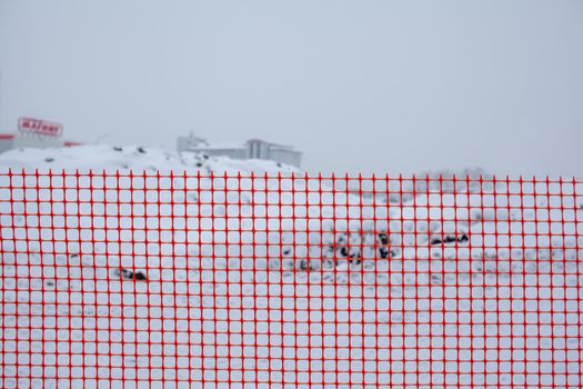 Plastic red safety net for construction site. Fencing repair work on the street. Construction grid on the background of winter snow