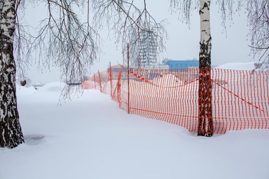 Plastic red safety net for construction site. Fencing repair work on the street. Construction grid on the background of winter snow