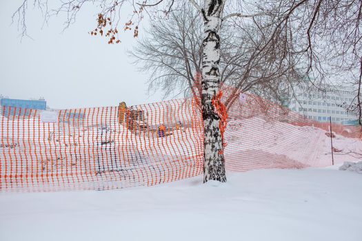 Plastic red safety net for construction site. Fencing repair work on the street. Construction grid on the background of winter snow