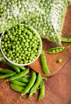 RAW baby peas in small white bowl, over retro wooden boards. Close-up