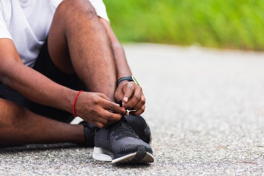 Close up Asian sport runner black man sitting shoelace trying running shoes getting ready for jogging and run at the outdoor street, health exercise workout concept