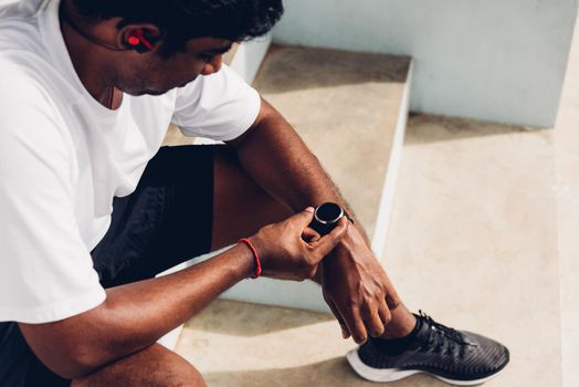 Close up Asian young athlete sport runner black man wear modern time smart watch he sitting resting before training running at the outdoor street health park, healthy exercise before workout concept