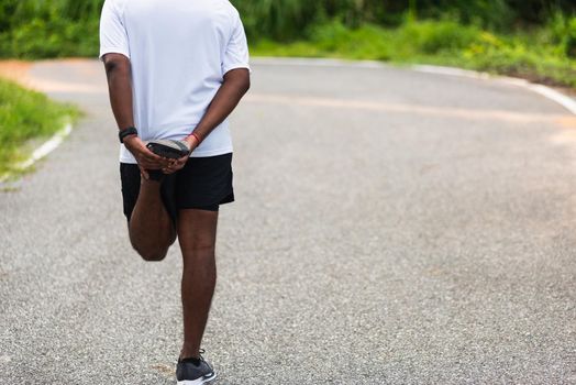 Close up Asian young athlete sport runner black man wear watch lift feet stretching legs and knee before running at the outdoor street health park, healthy exercise before workout concept