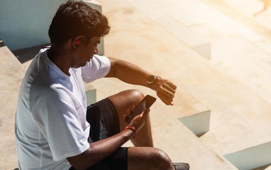 Close up Asian young athlete sport runner black man wear modern time smart watch and sync to a smartphone check running result after a training run at the outdoor, healthy exercise workout technology