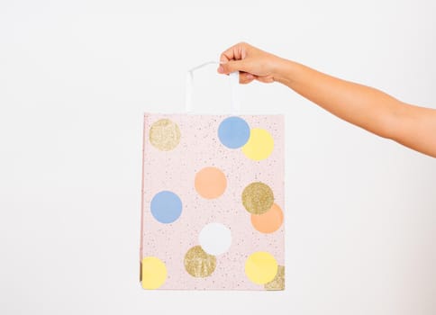 Closeup women hand holding a colorful pink shopping bag circular pattern, studio shot isolated on white background, female holds in hand white clear empty blank craft paper gift bag for purchases