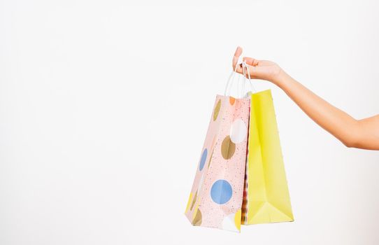 Closeup women hand holding colorful multicolor shopping bag many packets isolated on white background, female holds in hand white clear empty blank craft paper gift bag, shopping day concept