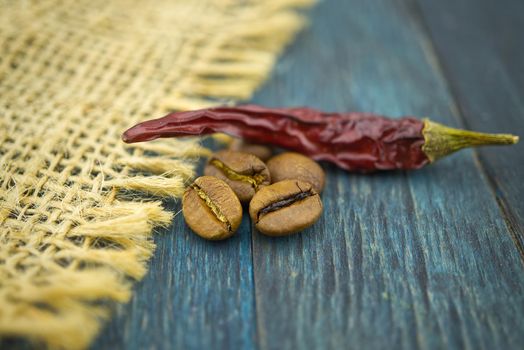 Macro photo of dried red chili pepper and roasted coffee beans on wooden and hessian or burlap fabric background