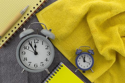 Color trends themed still life with alarm clock placed between of yellow wire bound notepads and pen on a textured grey background viewed as a flat lay from overhead