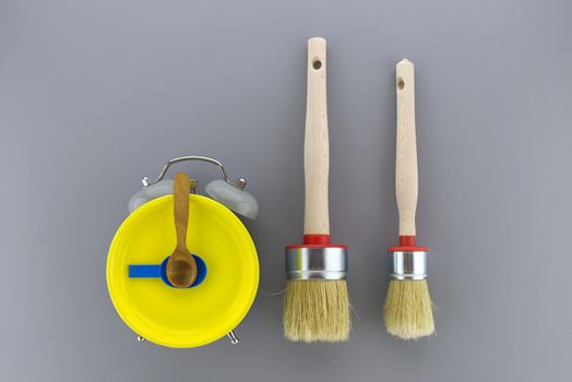 Creative DIY, decorating or renovations background with two clean bristle brushes and a colorful yellow alarm clock with tools for hands forming a border on grey with copy space