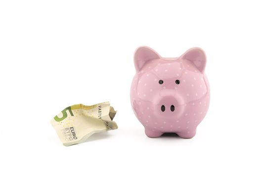 Crumpled banknotes of the euro and cute pink piggy bank on white with copy space for financial or savings concepts