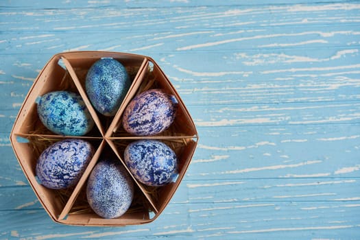 Blue chicken eggs lie in round wooden basket which stands on a blue wooden table. Easter background. Seasonal holiday flat lay with free space for text. Classic blue color of the year 2020