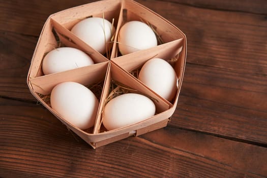 White chicken eggs lie in round wooden basket which stands on a dark wooden table. Easter background. Seasonal holiday flat lay with free space for text.