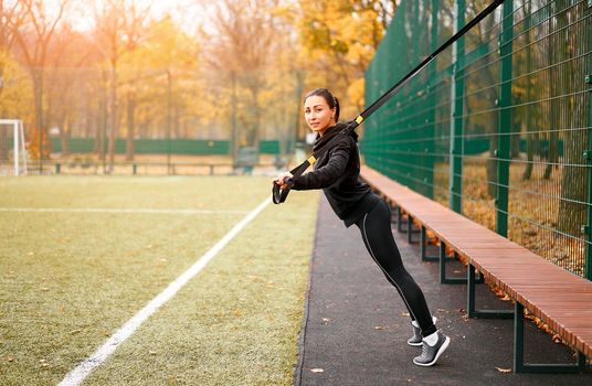 Girl athlete training sportground Mixed race young adult woman workout suspension system Healthy lifestyle Stretching outdoors playground. Make your body machine