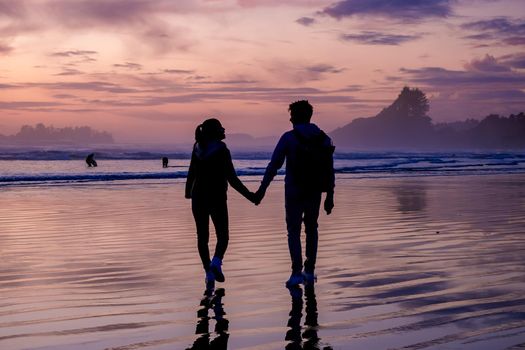 couple of men and women mid-age watching the sunset on the beach of Tofino Vancouver Island Canada, beautiful sunset on the beach with pink-purple colors in the sky. Canada Tofino