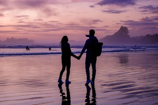 couple of men and women mid-age watching the sunset on the beach of Tofino Vancouver Island Canada, beautiful sunset on the beach with pink-purple colors in the sky. Canada Tofino