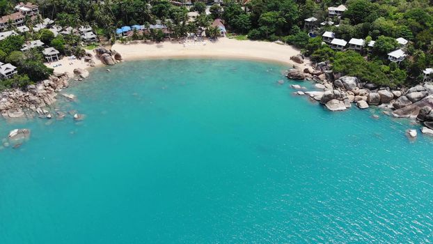 Small houses on tropical island. Tiny cozy bungalows located on shore of Koh Samui Island near calm sea on sunny day in Thailand. Volcanic rocks and cliffs drone top view