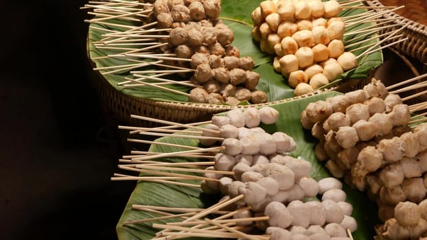 Baskets with BBQ meatballs on street. Stacks of delicious traditional barbecue meatballs on sticks placed on green palm leaves in baskets on street of Thailand