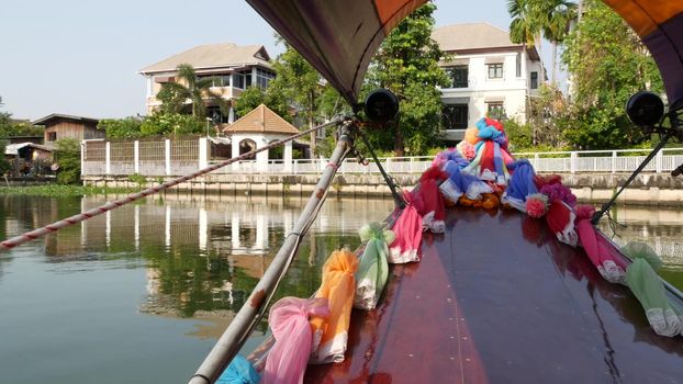 Tourist trip on Asian canal. View of calm channel and residential houses from decorated traditional Thai boat during tourist trip in Bangkok