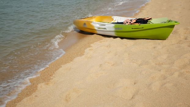 Kayak with paddles on sandy shore washed by waves of blue sea. Colorful canoe in wavy crystal water, tropical lonely island beach with copyspace. Outdoor activities, summer vacation, sport and health.