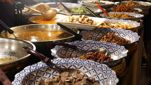 Bowls with various Asian dishes on stall. Bowls of assorted traditional Thai dishes placed on stall of street diner in evening. Oriental night market food court