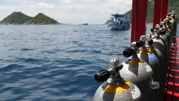 Row of oxygen tanks and diving equipment placed on modern boat in rippling ocean near Koh Tao resort, Thailand. Concept of tourist sports extreme entertainment, adventure and new experience