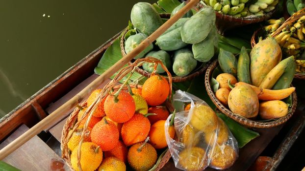 Iconic asian Lat Mayom floating market. Khlong river canal, long-tail boat with tropical exotic colorful fruits, organic locally grown vegetables. Top view of harvest and street food in wooden canoe.