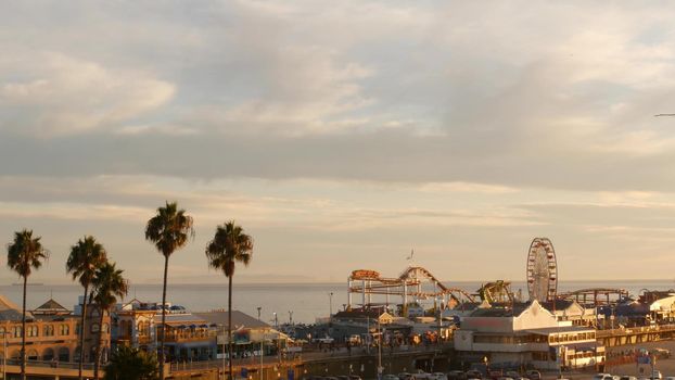 Classic ferris wheel, amusement park on pier in Santa Monica pacific ocean beach resort. Summertime California aesthetic, iconic view, symbol of Los Angeles, CA USA. Sunset golden sky and attractions.