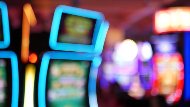 Defocused slot machines glow in casino on fabulous Las Vegas Strip, USA. Blurred gambling jackpot slots in hotel near Fremont street. Illuminated neon fruit machine for risk money playing and betting.