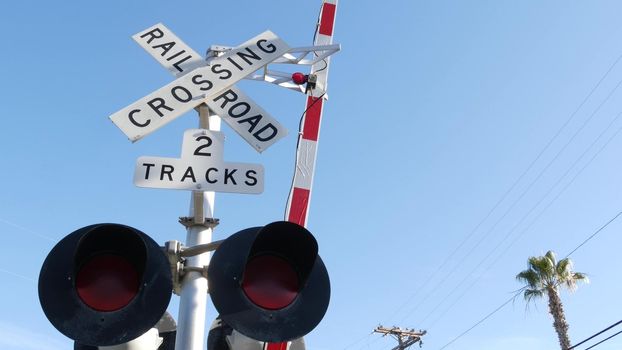 Level crossing warning signal in USA. Crossbuck notice and red traffic light on rail road intersection in California. Railway transportation safety symbol. Caution sign about hazard and train track.