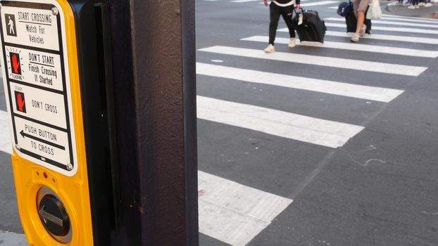 Traffic light button on pedestrian crosswalk, people have to push and wait. Traffic rules and regulations for public safety in USA. Zebra street crossing on road intesection in San Diego, California.