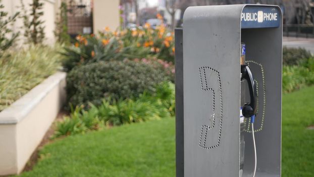 Retro coin-operated payphone station for emergency call on street, California USA. Public analog pay phone booth. Outdated technology for connection and telecommunication service. Cell handset on box.