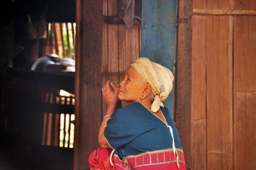 CHIANG MAI, THAILAND - MARCH 1, 2013: Side view of elderly woman of Lisu people sitting on porch of house looking away in rest, Thailand. Senior woman of ethnic Asian tribe