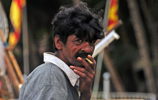 HIKKADUVA, SRI LANKA - 21th DEC, 2011: Indian mature fisherman smoking outdoors, portrait, Mature ethnic man smoking cigarette and looking at camera, Sri Lanka beach