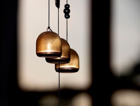 Three brass door bells (wind chimes) against the background of the window.