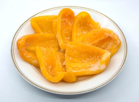 On a white plate lies frozen yellow bell pepper sliced into wedges.