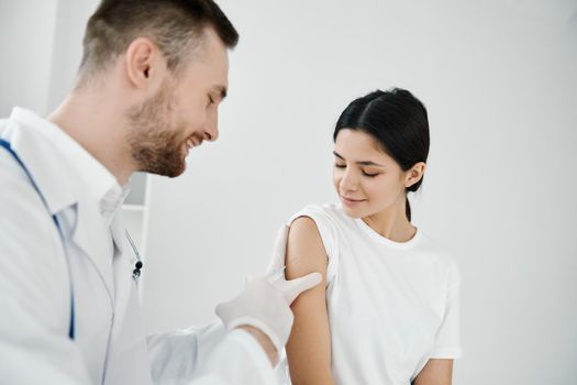 doctor with a stethoscope makes an injection into the shoulder of a woman patient on a light background. High quality photo