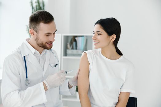 a professional doctor injects a vaccine into the shoulder of a woman in a white t-shirt on a light background. High quality photo