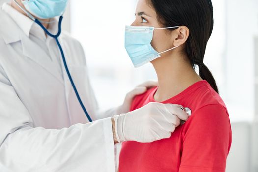 doctor in a medical mask and a dressing gown examine a woman in a t-shirt . High quality photo